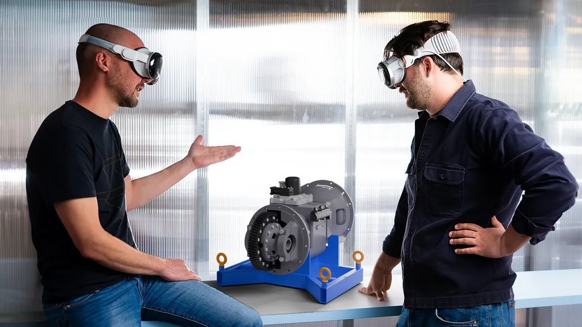 two people wearing goggles standing next to a 3D printed equipment.