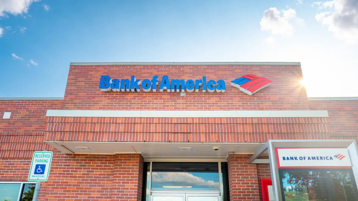 A bank branch building features the "Bank of America" name and logo in front of sunny skies.