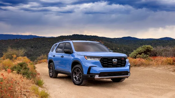 A blue 2023 Honda Pilot TrailSport SUV on a dirt road with hills in the background.