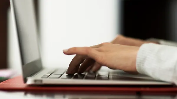 A close up of hands on a keyboard of a laptop. The laptop is sitting on a book on a table