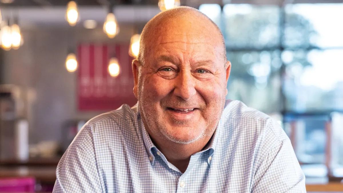 A photograph of a person in a button down shirt smiling at the camera.