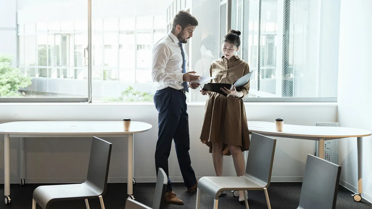 Two business people in a meeting office standing, talking, and looking over documents