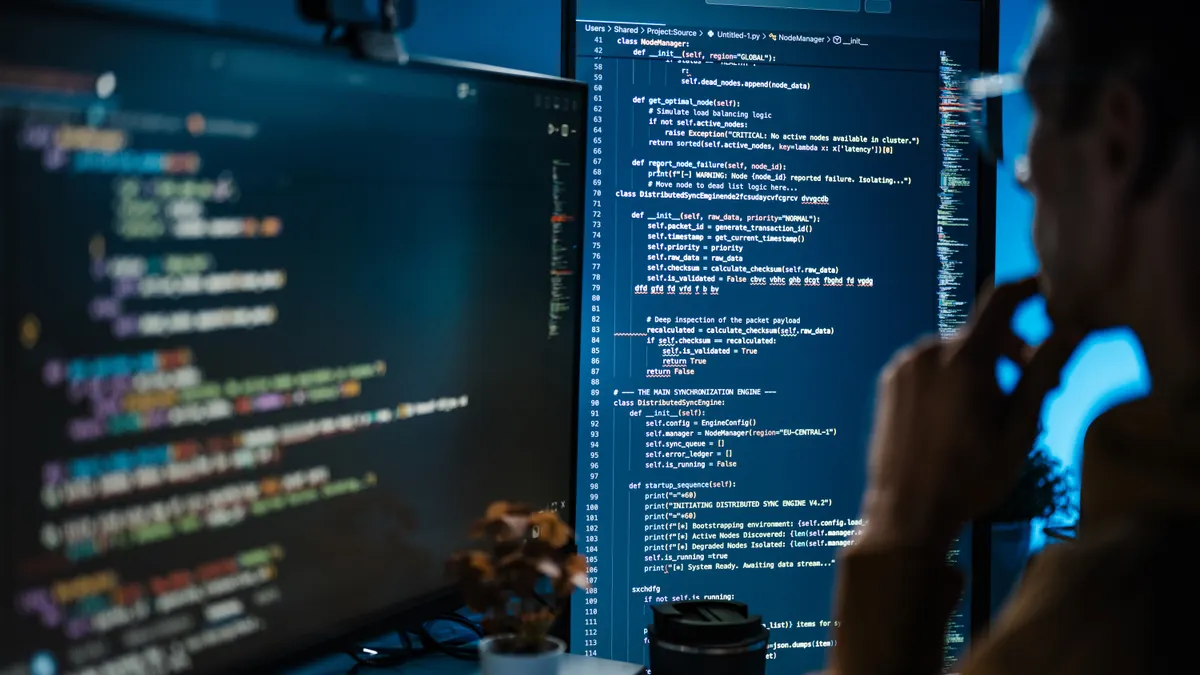 A Software Developer Reviews Source Code on Large computer Screen.