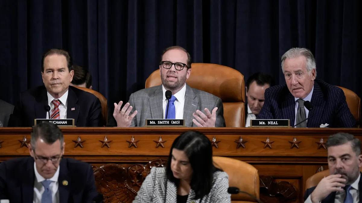 Committee Chair Jason Smith is seated speaking center with ranking member Richard Neal on his left, photo right, and Vern Buchanan to the right, photo left. Three reps out of focus below.