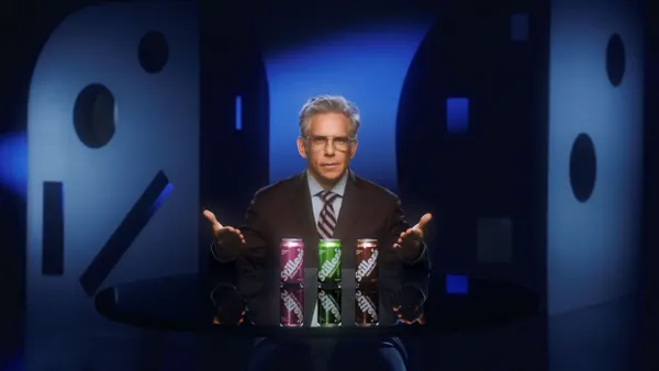 Ben Stiller sits behind a desk on which are three cans of soda.