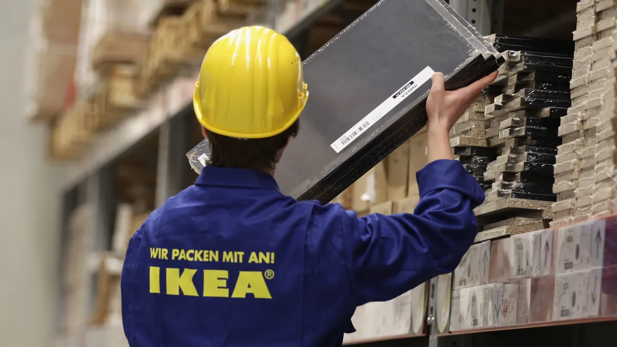 A man in a blue uniform and yellow hard hat removes a package from a shelf.