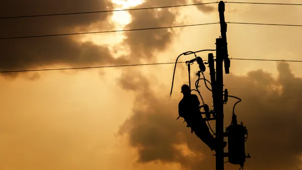 The silhouette of a power line worker climbing on an electric pole replacing a damaged line.