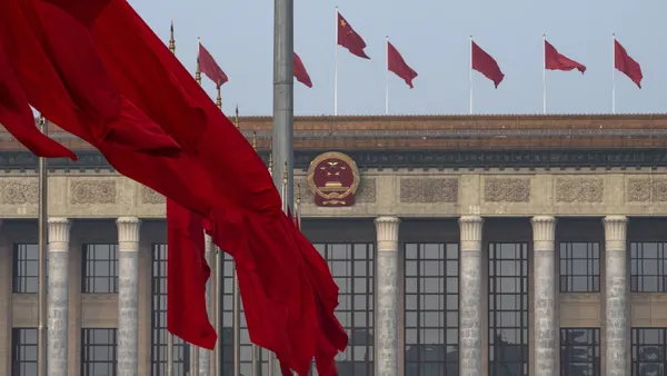 A Chinese flag flutters in front of a Chinese government building, on top of which other Chinese flags are flying