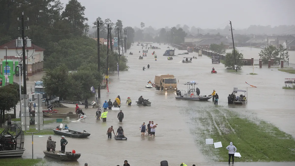 A flooded street with people, boats and vehicles.