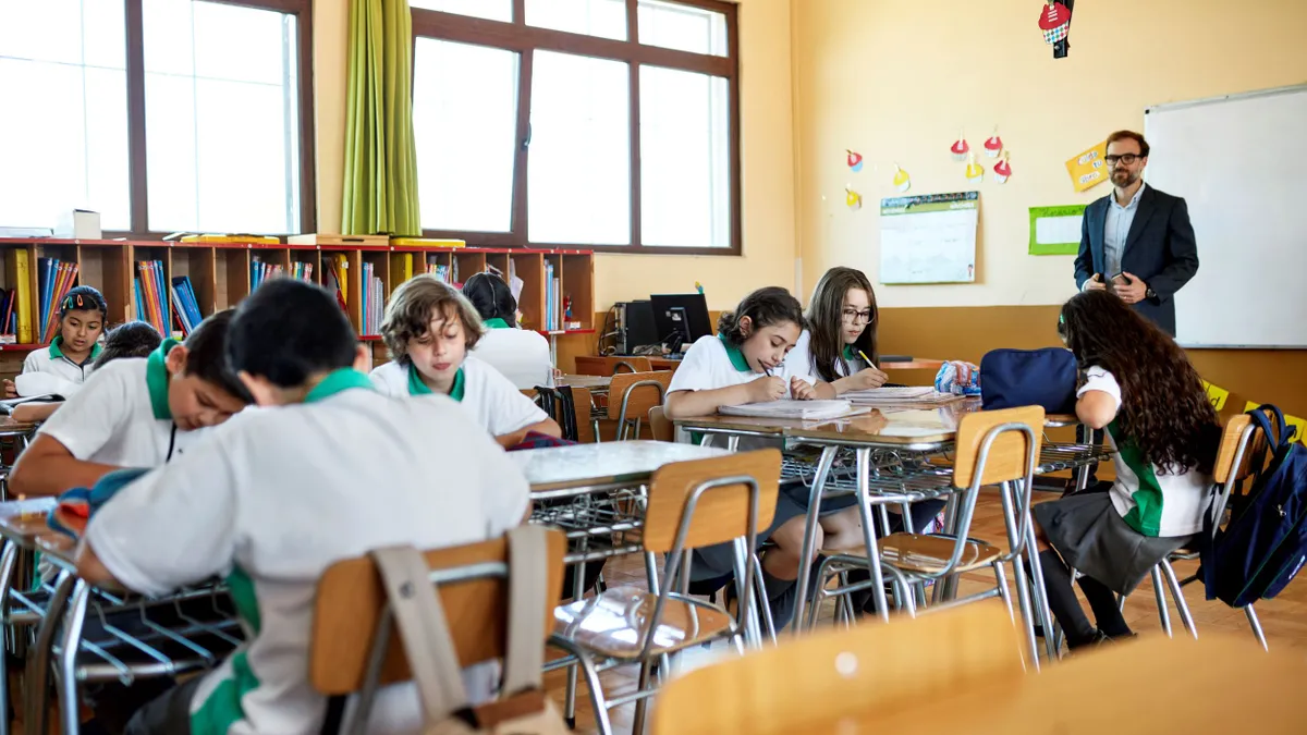 A teacher is standing while instructing in front of a classroom of students.