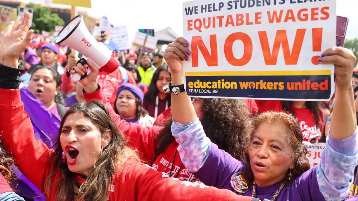 Two individuals are see participating in a strike. One holds a sign that says "We help students learn. Equitable wages now."