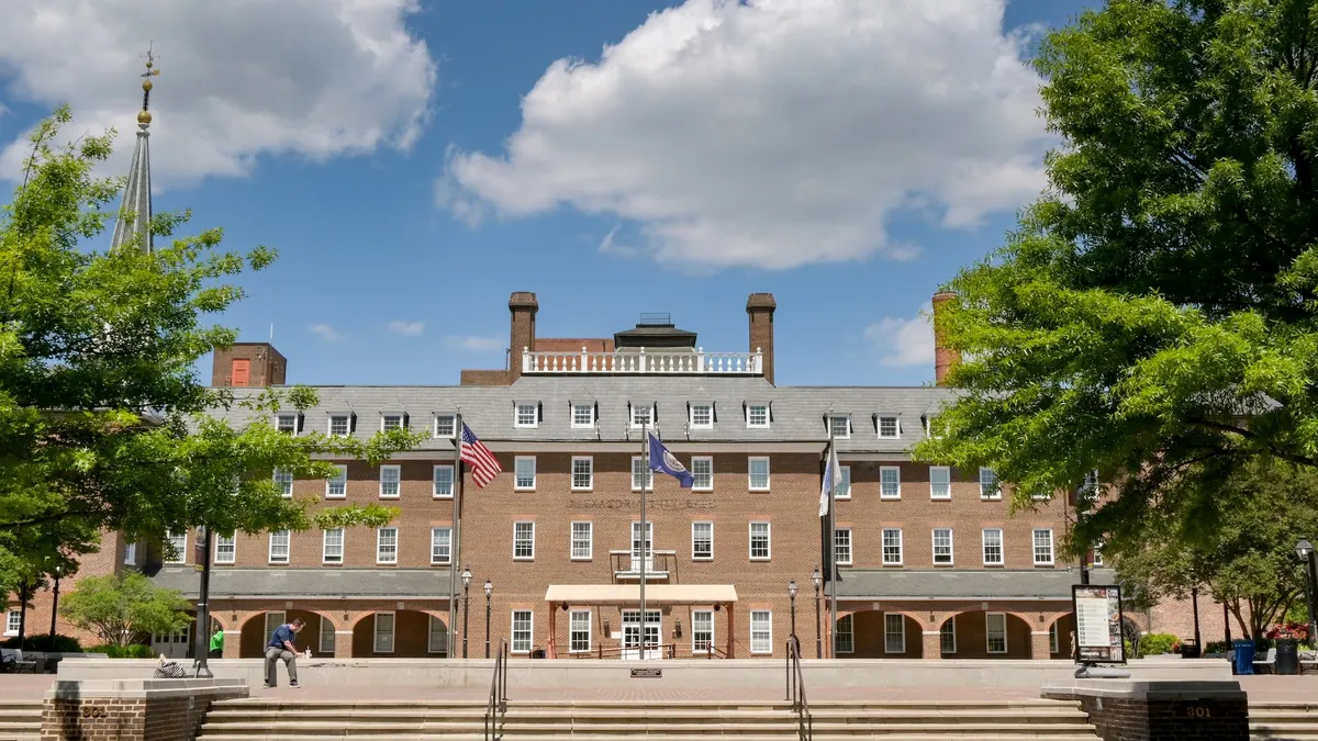 The front of a large brick building with flags in front of it.