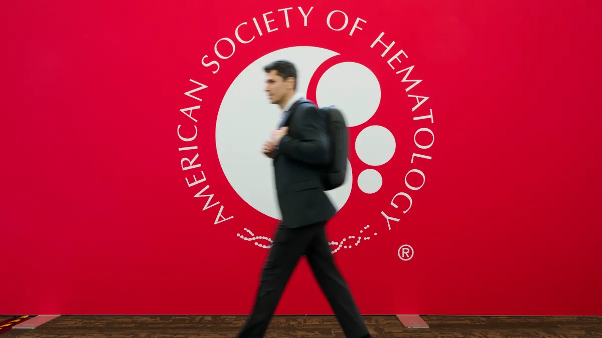 A man in a suit walks by a sign that reads American Society of Hematology