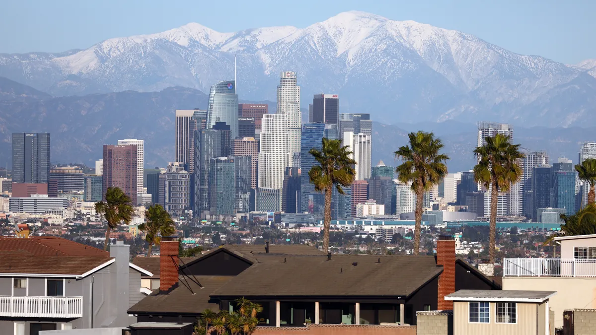 Homes and palm trees in the foreground, with the Los Angeles skyline and San Gabriel Mountains in the background