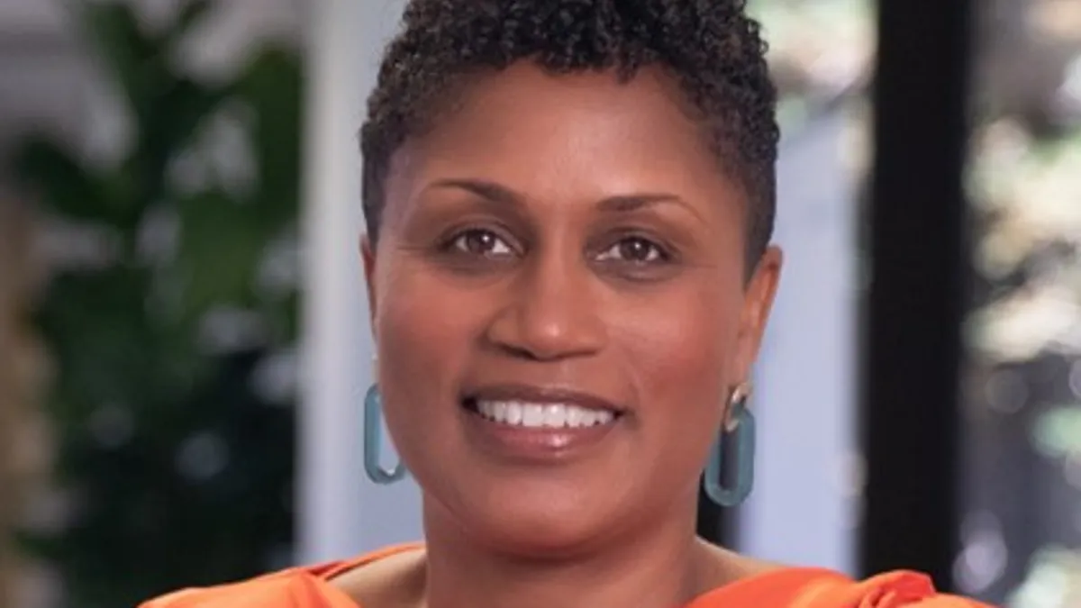 A headshot of Jennifer Jones-McMeans, who is smiling in the photo. She is wearing an orange blouse and blue hoop earrings.