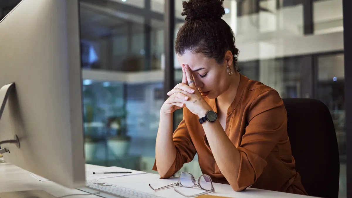 Person sitting at a desk with her hands on their forehead.