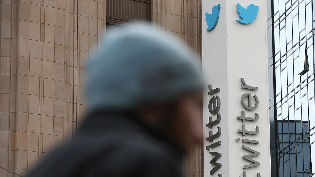 Medium shot of Twitter headquarters' @twitter sign; a person, blurred, passes in front of the camera