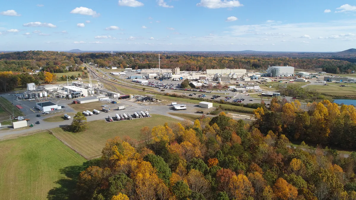 A white building surrounded by a parking lot filled with cars and green landscape on a sunny day.