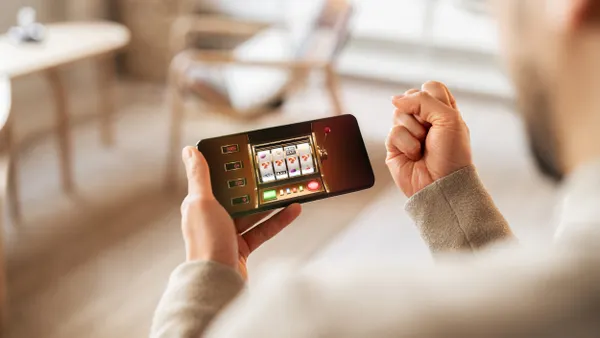A close-up view of an individual holding a smartphone displaying a slot machine game, celebrating a winning outcome indoors.