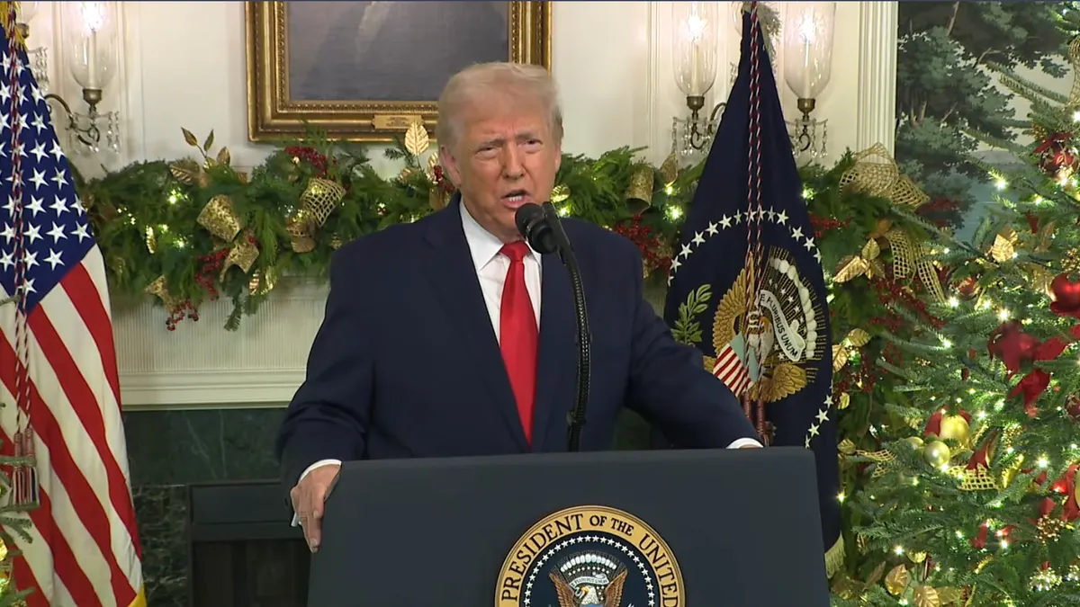 President Donald Trump stands at a podium in the White House, surrounded by Christmas decor.