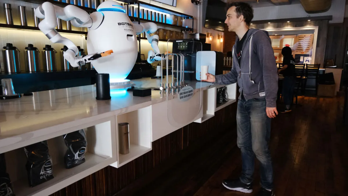 A smiling man approaches a white counter where a white robot is preparing an espresso drink.