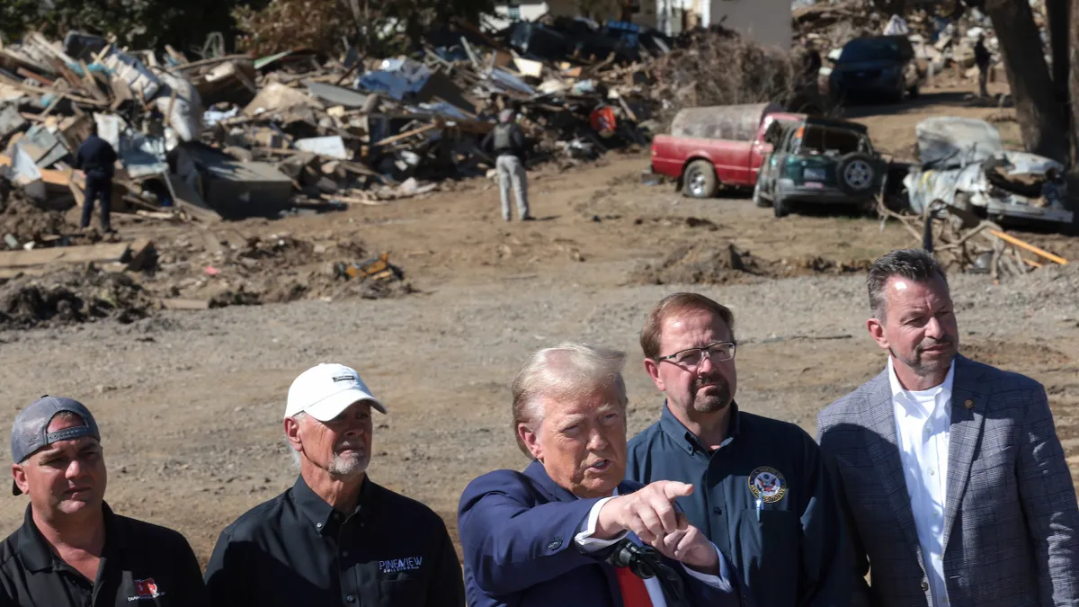 President Trump standing with a group of men and pointing his finger in front of a pile of rubble.