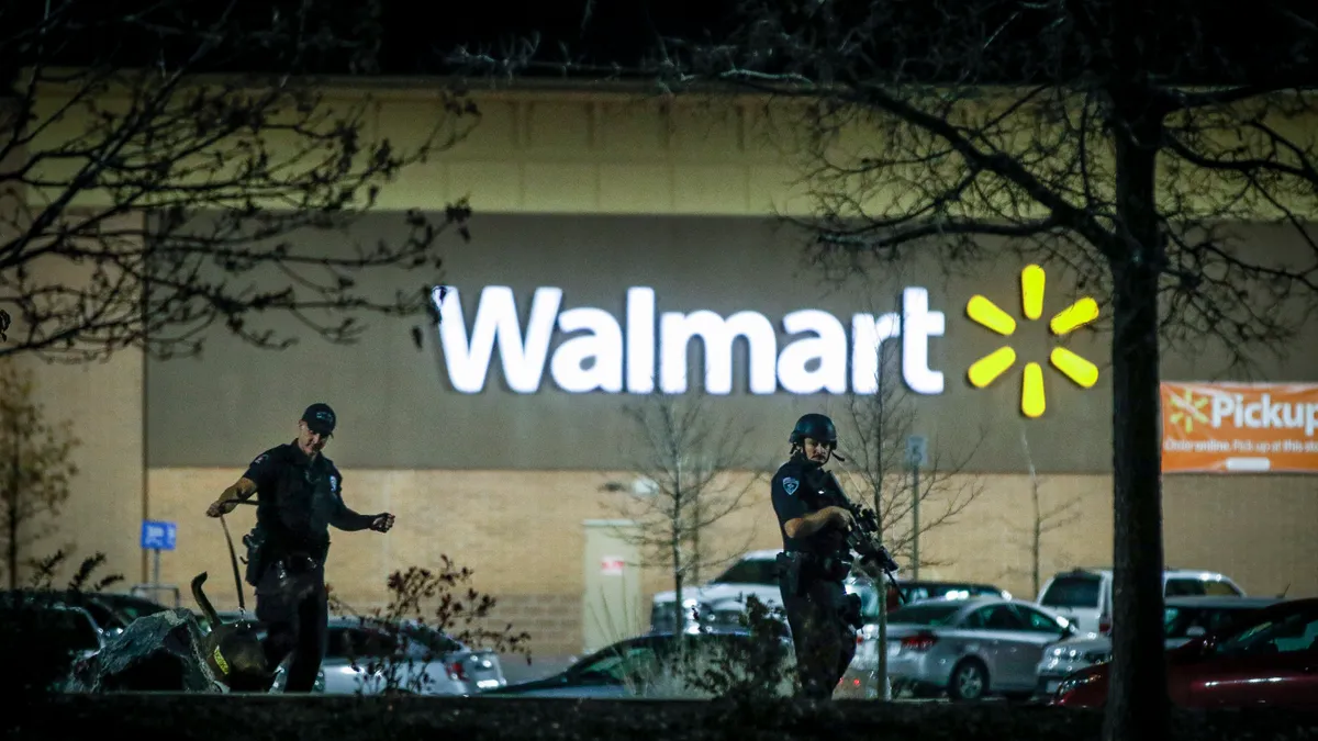 Two police officers in front of a big box store, amid trees and cars.