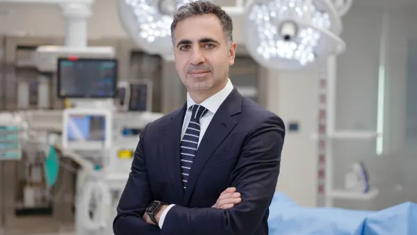 A picture of a man in a suit with his arms crossed standing in a hospital operating room.