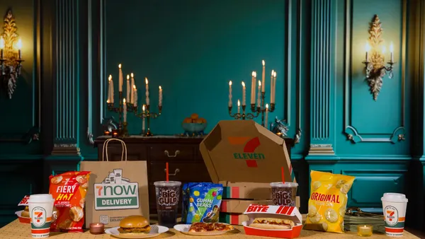 A table is set with an array of food and beverage items in a room with candlelight and dark green walls.
