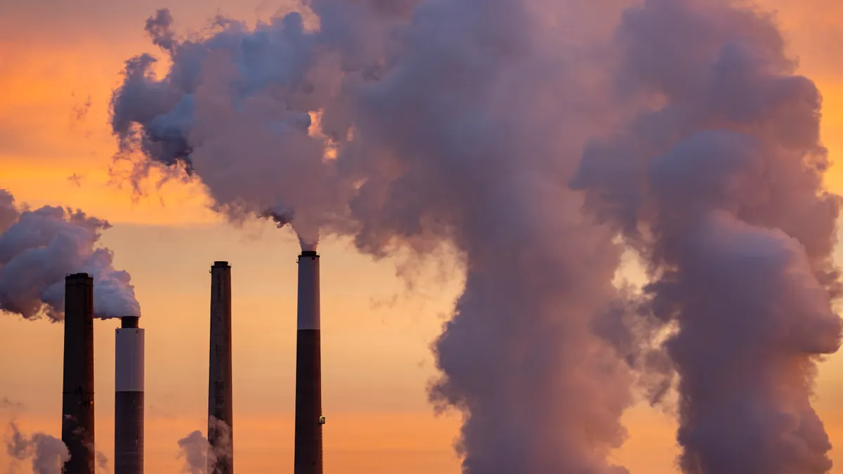 Smoke and steam pouring from smokestacks with orange sky in background.