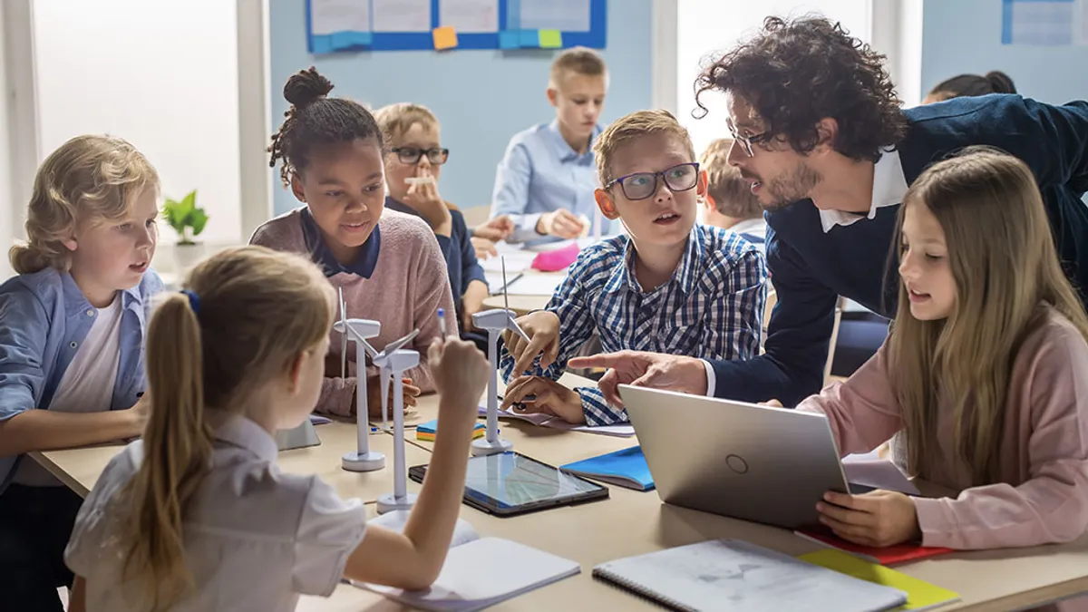 A teacher talking to a young group of grade school students that are working on a class project