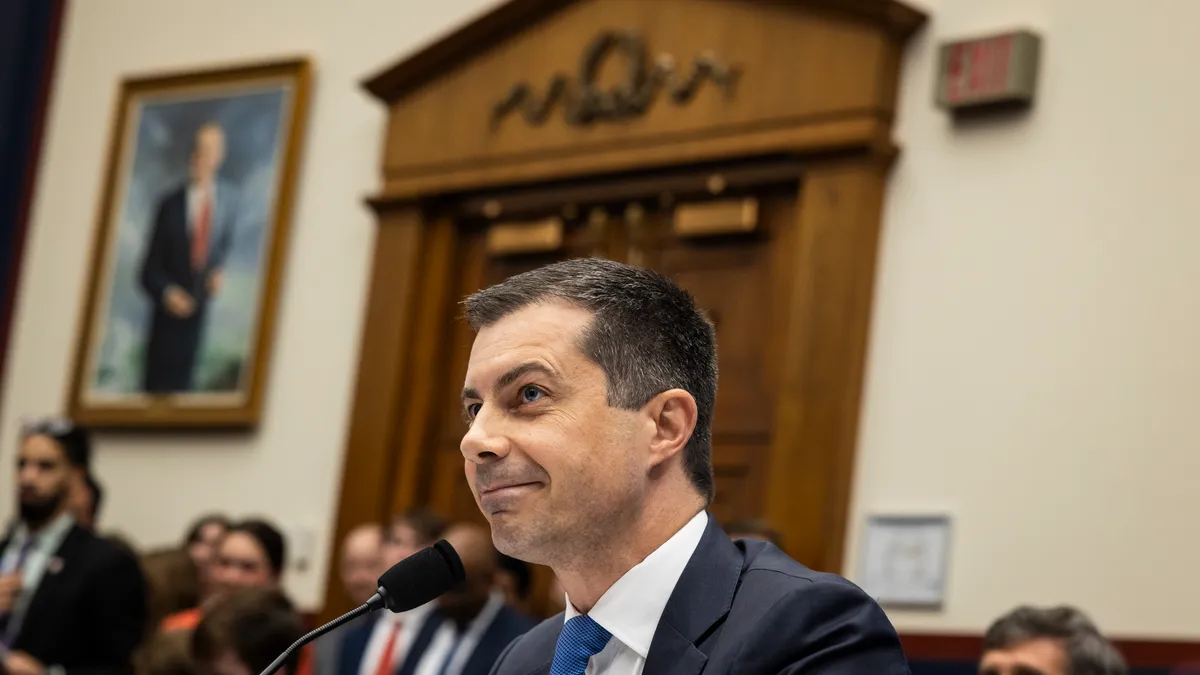 U.S. Secretary of Transportation Pete Buttigieg in front of a microphone in a U.S. Capitol hearing room.