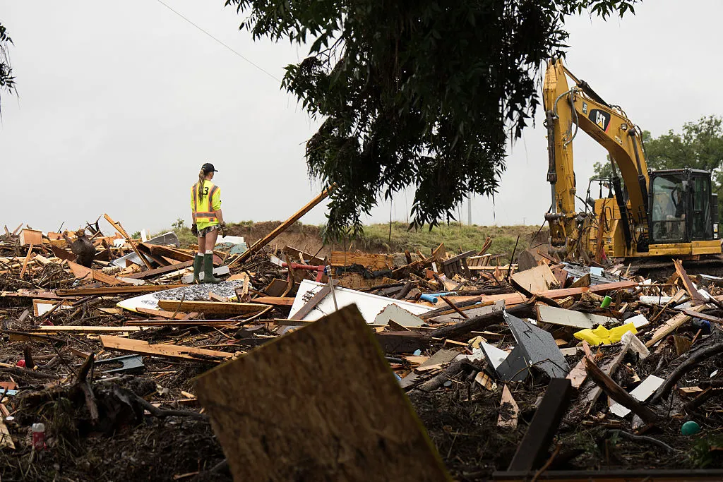 Workers operate heavy machinery to clear debris after massive flooding on July 6, 2025 in Hunt, Texas. A worker stood on debris from a structure.