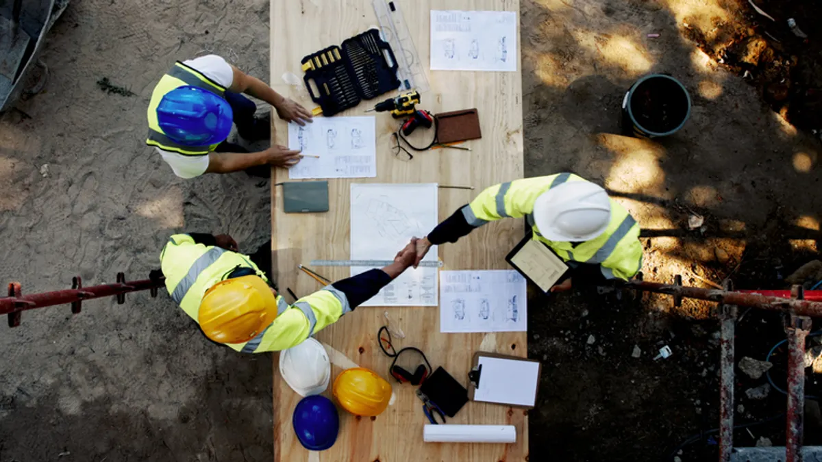 A group of construction workers shake hands over blueprints.
