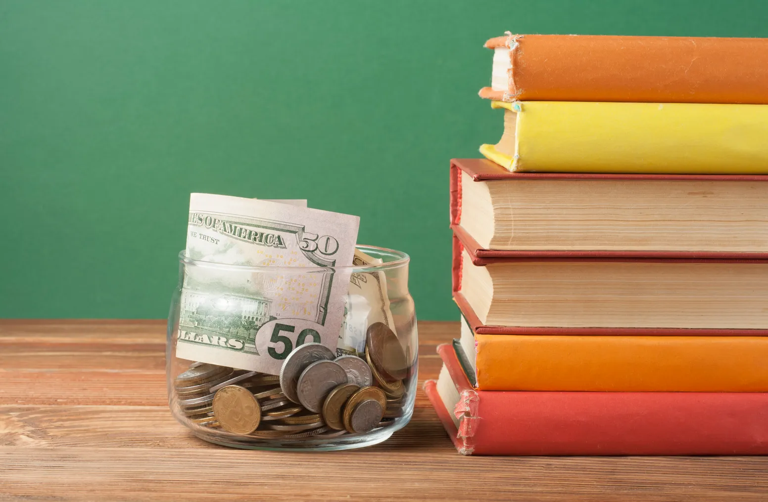 A jar of cash sits next to a stack of books on a teacher's desk.