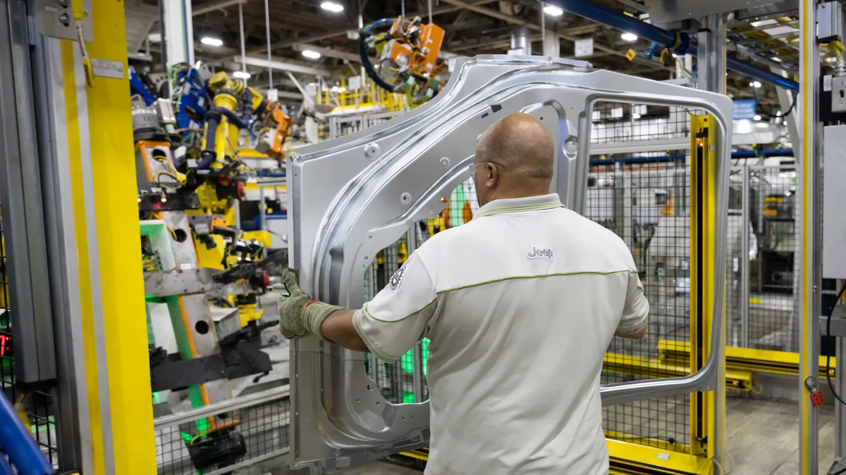 A production operator at Stellantis' Detroit Assembly Complex loads a door frame for a Jeep Grand Cherokee.