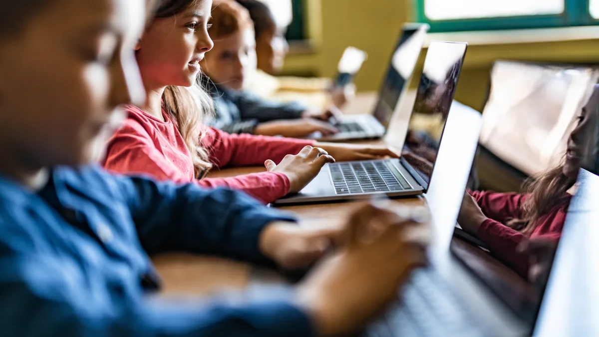 A row of elementary students work on their computers side by side in a classroom.