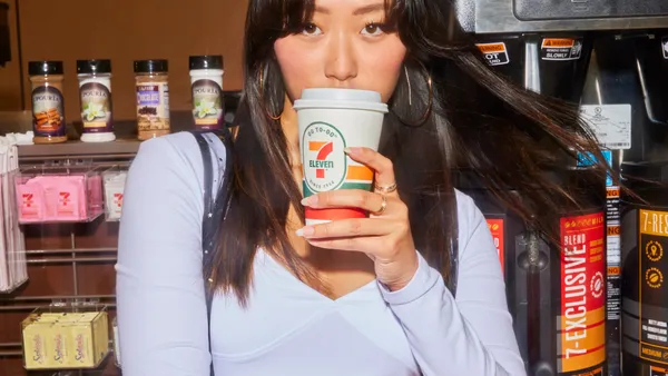 A person drinks from a 7-Eleven-branded hot beverage cup.