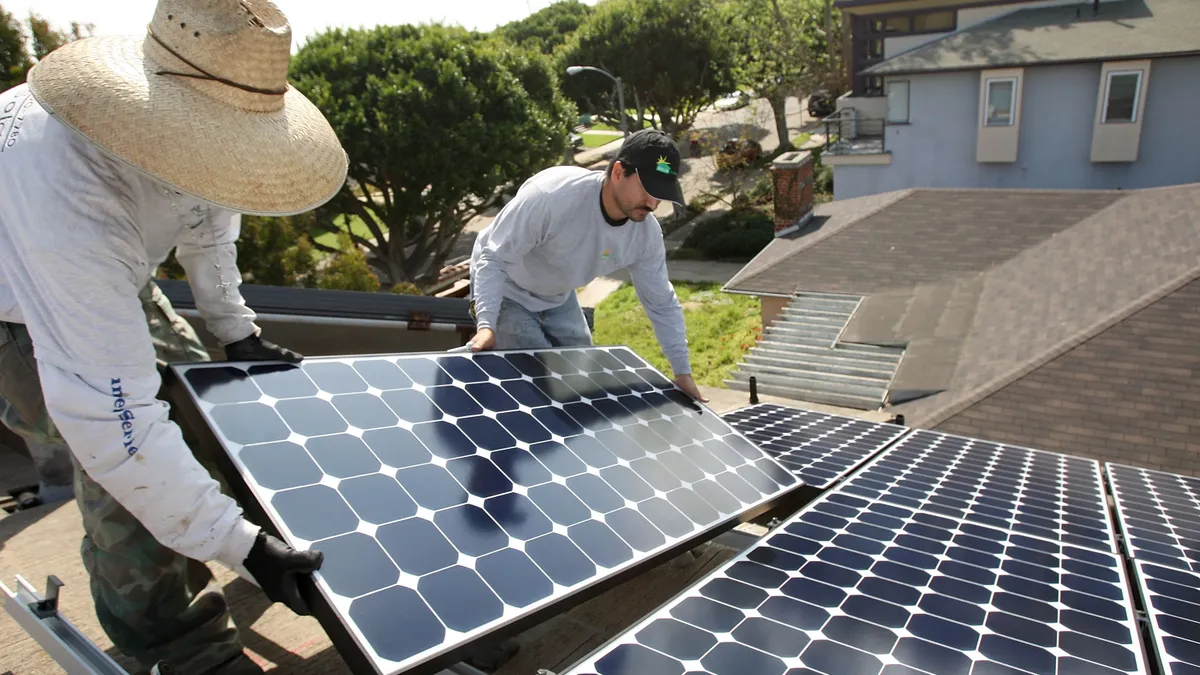 Two people install a solar panel on a roof.