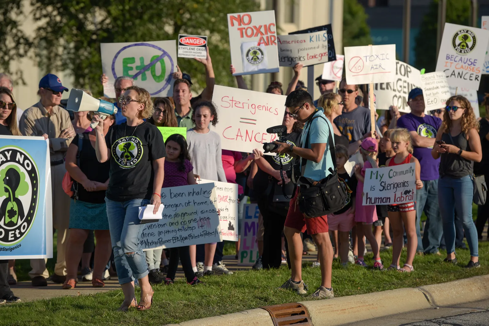 A person holding a megaphone is surrounded by people holding signs that read "No toxic air" and "Sterigenics = Cancer"