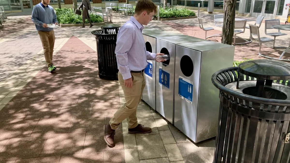 A person putting a plastic bottle into a recycling bin.