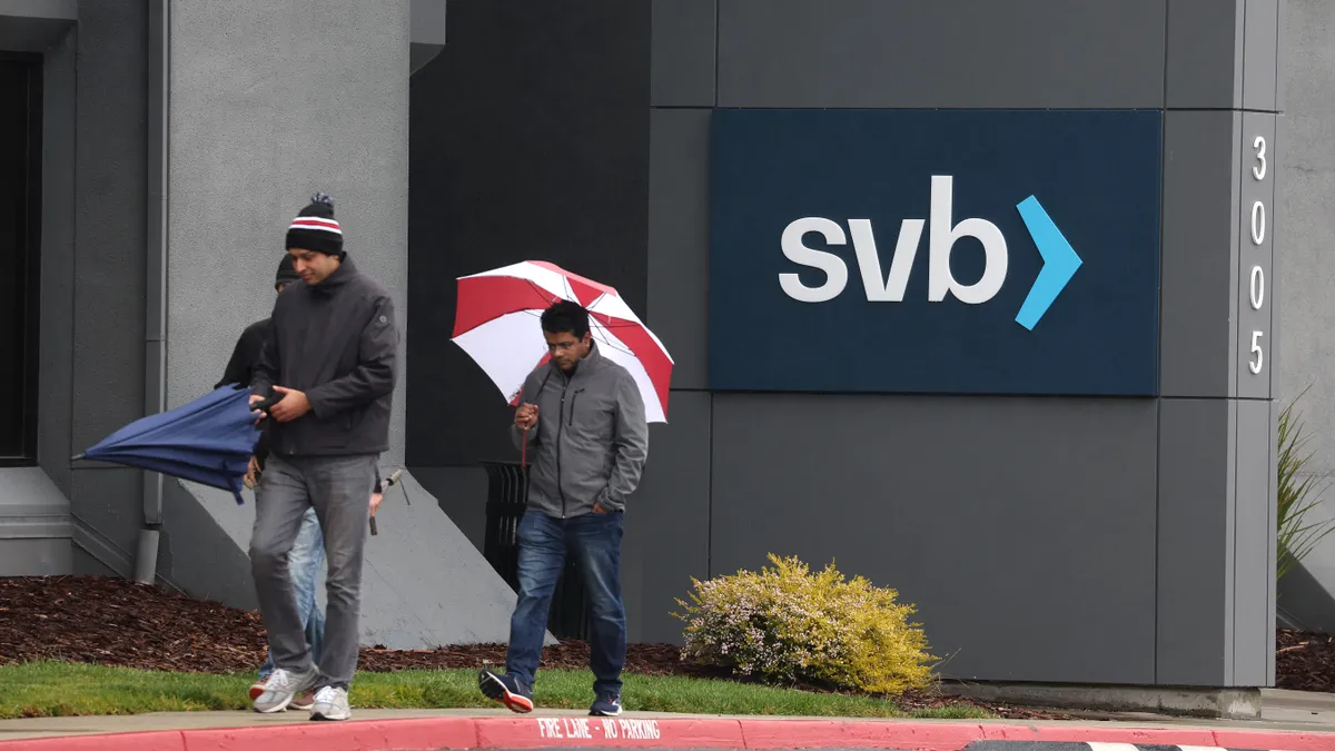 Employees walk in front of a sign outside of the shuttered Silicon Valley Bank headquarters.