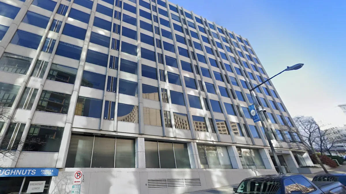 A white stone and glass building with cars parked at the bottom.