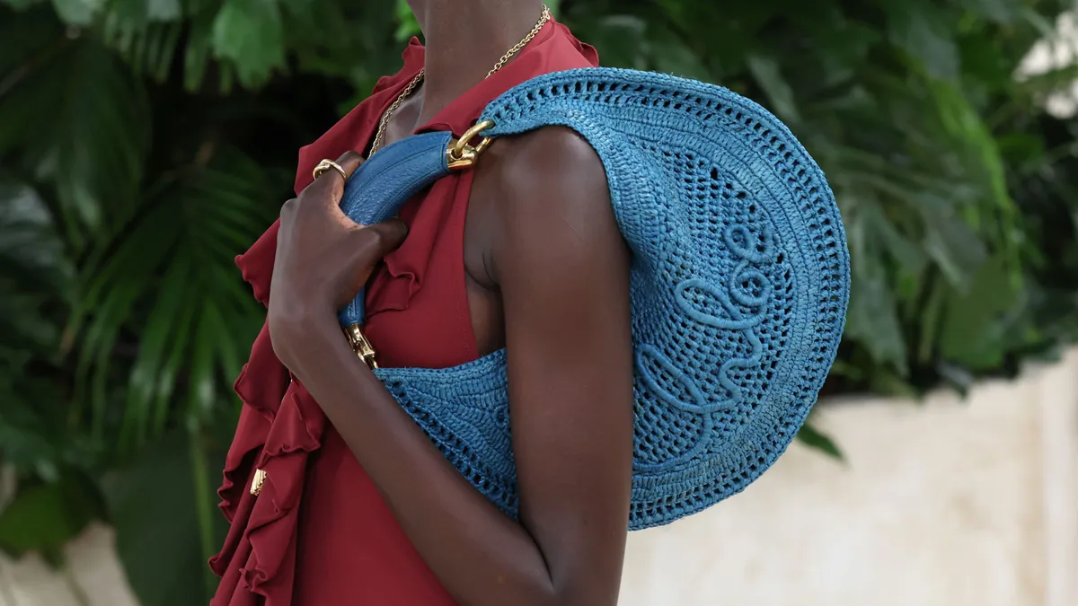 A model holds a blue shoulder bag with the word Chloé written on the side of the bag.