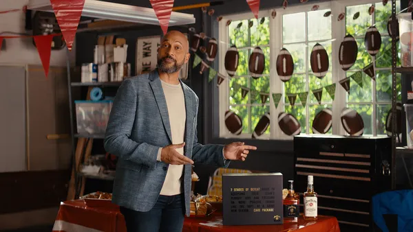 Keegan-Michael Key wears a blue sports coat near a football banner and Jim Beam care package.