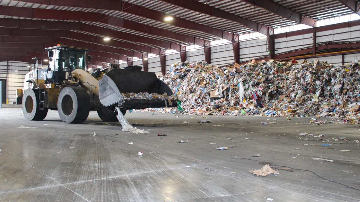 A front enloader moves recyclables into piles in a warehouse where material is stored.