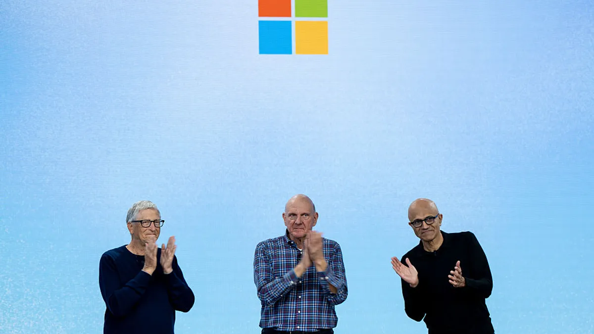 Three men pose together, arms linked, in front of a crowd in the foreground that snaps photos with their phones.