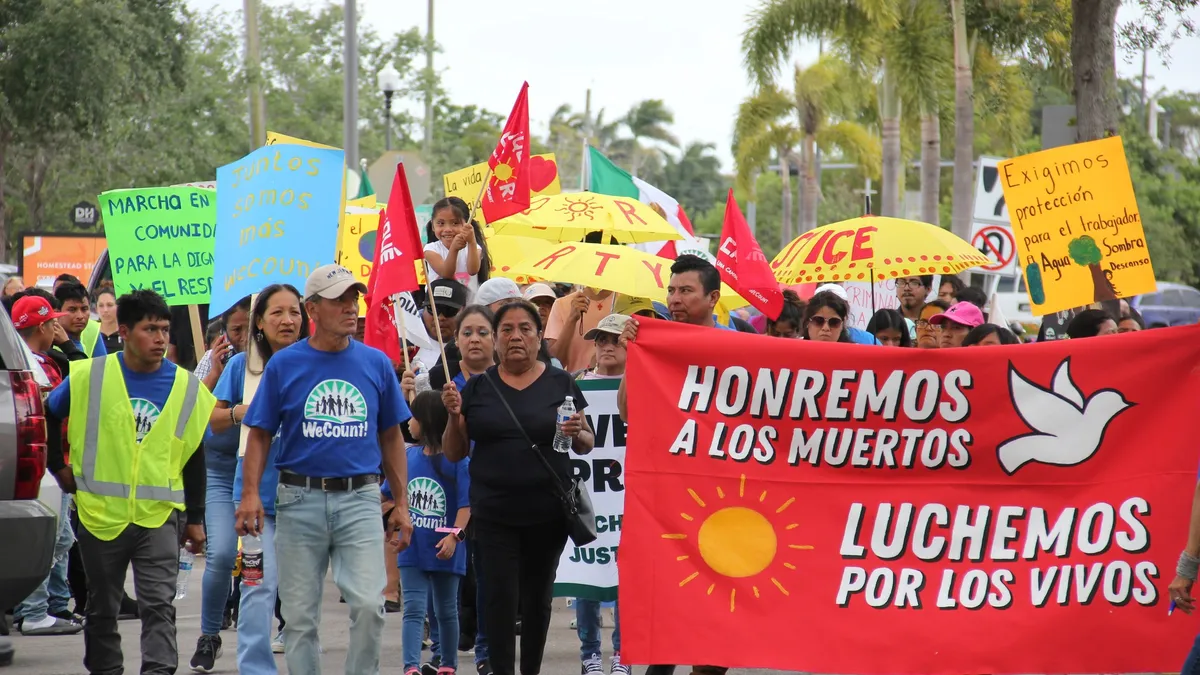 A group of people holding signs written in Spanish march through a street.