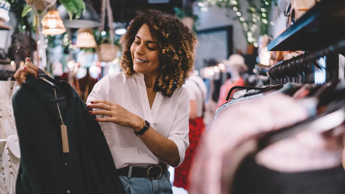 Female standing near hangers with brand wear and laughing during shopping