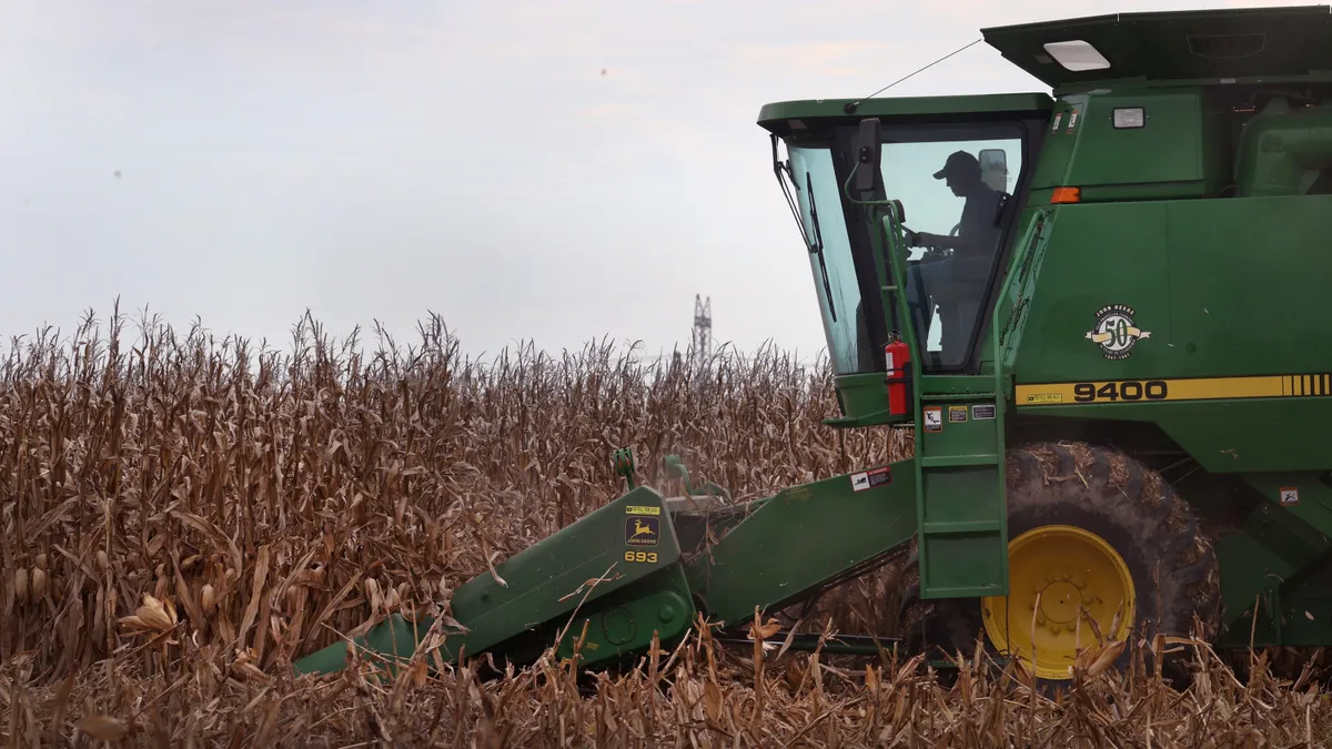 The silhouette of a farmer is seen inside a tractor as he harvests corn